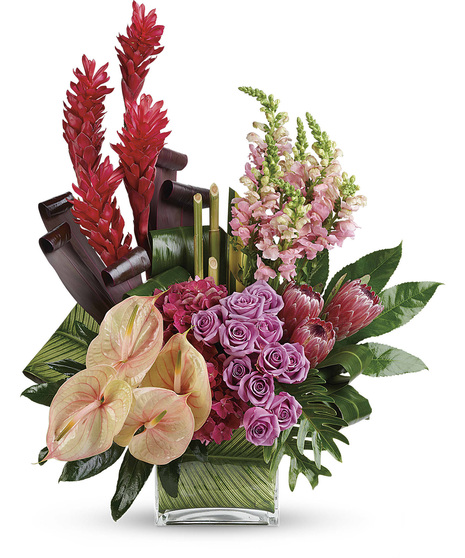 Bouquet of mixed tropical flowers and greenery in a leaf-lined glass cube vase